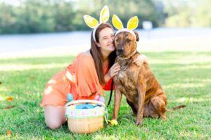 Brunette girl wearing orange strapless romper from red dress boutique and Easter bunny ears with brindle rescue dog and diy dog easter basket