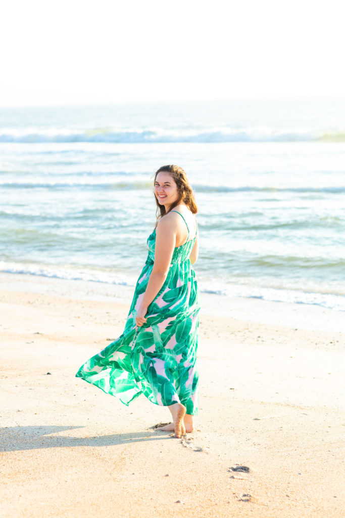 Brunette-Girl-Wearing-BuddyLove-Sirens-Song-Green-And-Pink-Tropical-Print-Maxi-Dress-With-Pink-Wicker-Round-Bag-At-Florida-Beach