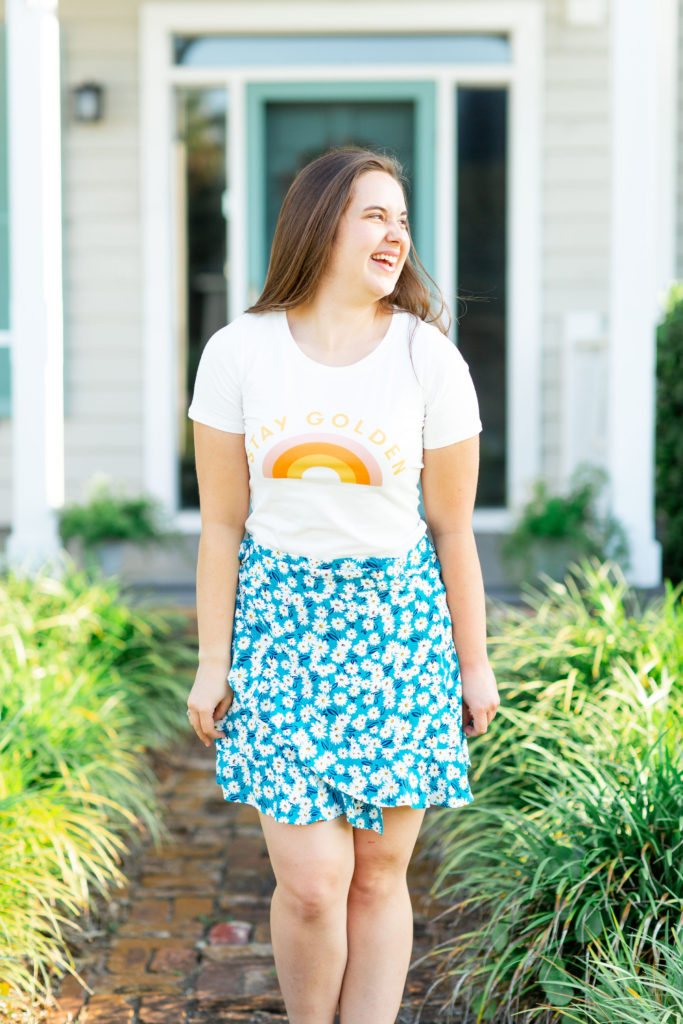Brunette-Girl-Wearing-Stay-Golden-Graphic-Tee-And-Blue-Floral-Wrap-Skirt-From-Madison-And-Mallory