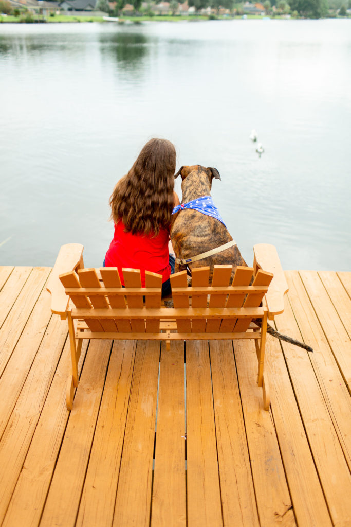 Brunette-Girl-And-Brindle-Rescue-Dog-Sitting-On-Bench-On-Lake-Dock
