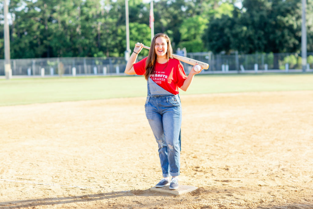 Brunette-Girl-Wearing-Charlie-Southern-Baseball-Graphic-Tee-And-Blue-Overalls-From-Red-Dress-Boutique-And-Vans-Sneakers-With-Louisville-Slugger-Baseball-Bat-And-Baseball